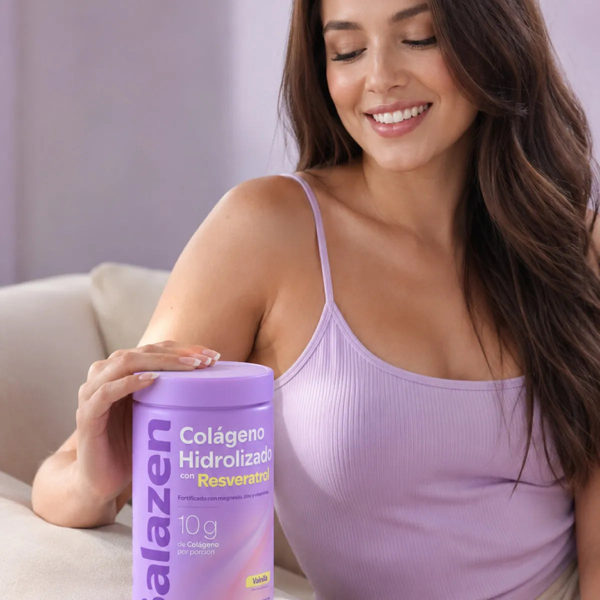 Mujer sonriente y feliz sosteniendo un envase de Colágeno Hidrolizado Balazen con Resveratrol Vainilla en un sofá.